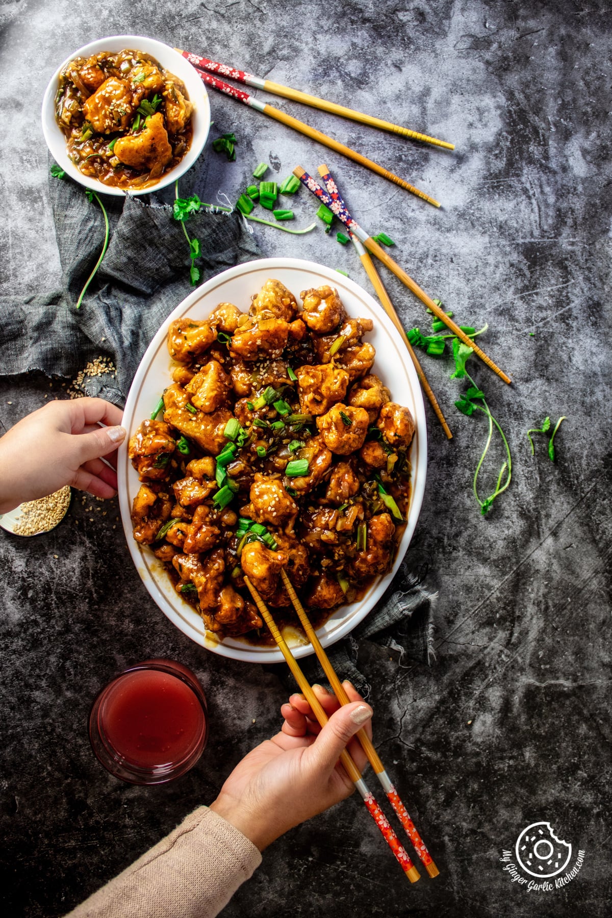 overhead shot of gobi manchurian a white oval plate where female hands holding wooden chopsticks